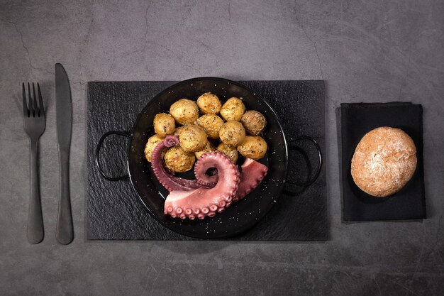 Stew octopus tentacles with potatoes on a skillet plate on dark background Top view.