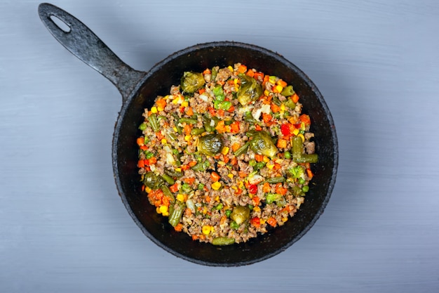 Stew with assorted vegetables and meat in a pan on a gray background, top view.