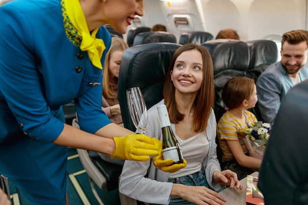 Stewardess giving champagne to joyful woman in airplane