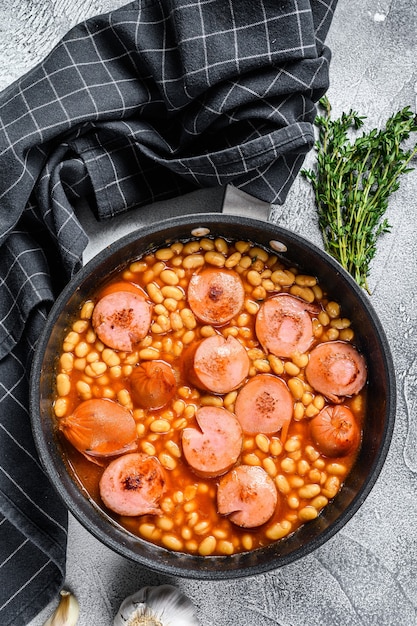 Photo stewed beans with smoked sausage and tomato sauce in a pan.   top view.