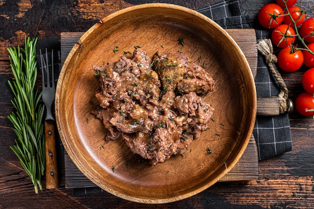 Stewed beef meat in a wooden plate. Dark Wooden background. Top view.