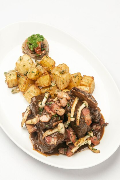 Stewed beef short ribs and mushrooms in gravy with roast potatoes on white background