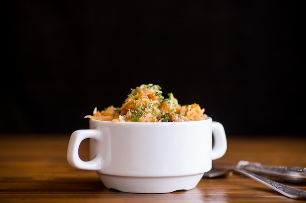 stewed cabbage with carrots and spices in a bowl on a black background