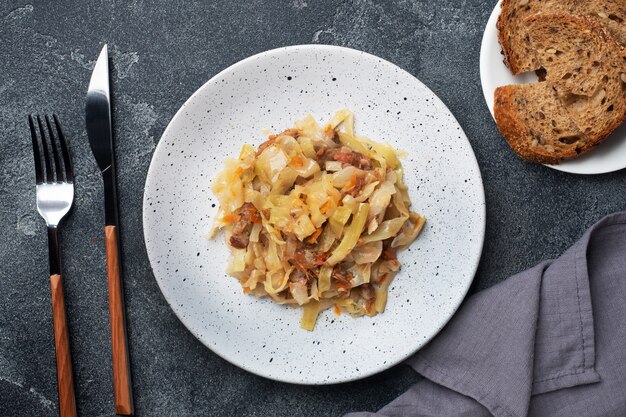 Stewed cabbage with meat on a plate. Dark concrete background.