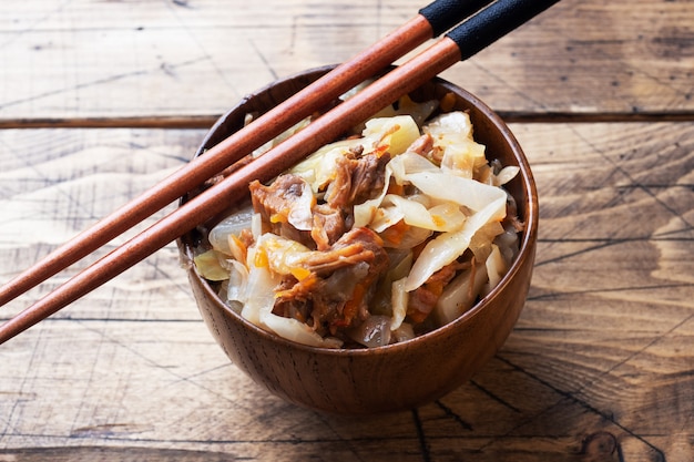 Stewed cabbage with meat in a wooden bowl on a wooden background. Traditional Russian dish of Solyanka.