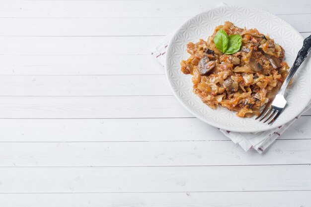 Stewed cabbage with mushrooms on white wooden background Copy space