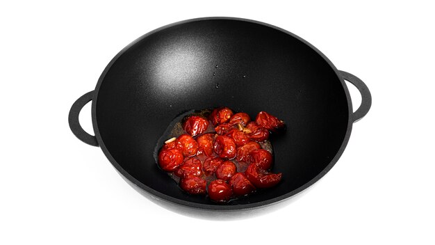 Stewed cherry tomatoes with garlic in a wok pan isolated on a white background. Preparation of bucatini pasta. High quality photo