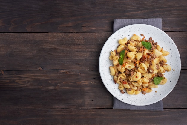 Stewed pasta with minced beef and vegetables, macaroni in Navy style on a plate. Dark wooden background. Copy space.