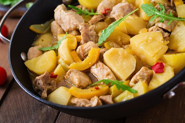 Photo stewed potatoes with meat and vegetables in a roasting tin on a wooden background