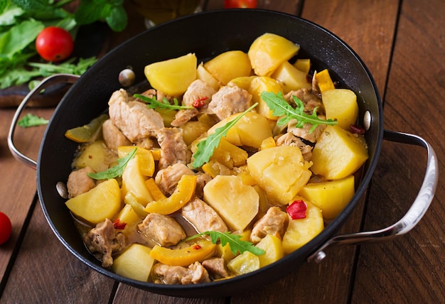 Photo stewed potatoes with meat and vegetables in a roasting tin on a wooden background