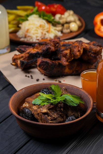 Stewed ribs with prunes in plate with wine on black wooden background