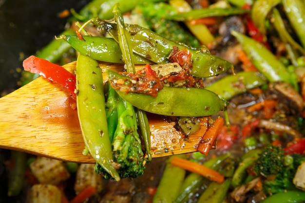 Stewed vegetables broccoli tomatoes and green peas with a wooden spoon closeup