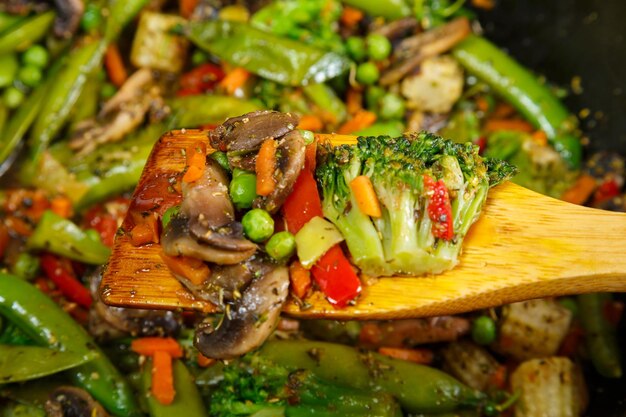 Stewed vegetables broccoli tomatoes and green peas with a wooden spoon