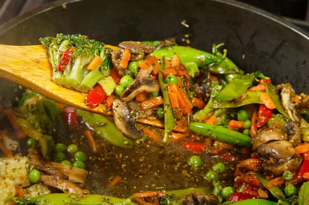 Stewed vegetables broccoli tomatoes and green peas with a wooden spoon