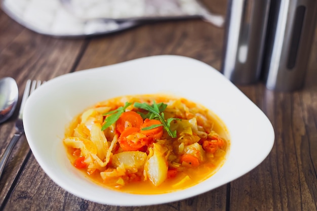 Stewed vegetables in a white bowl on wooden table selected focus