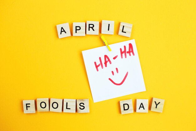 Photo sticker with smiley and inscription april fools day made by wooden cubes on yellow background