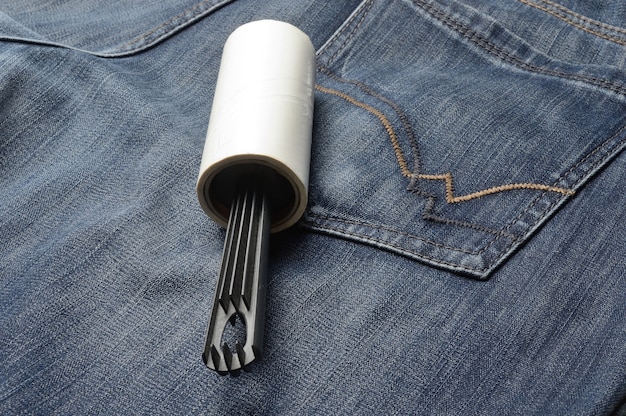 A sticky, roller-coiled garment brush rests on dark jeans.