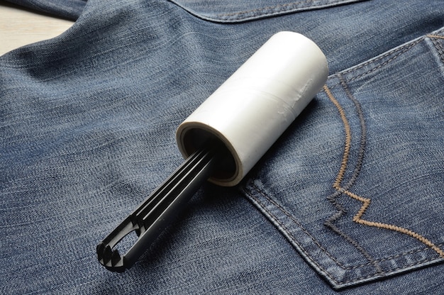 A sticky, roller-coiled garment brush rests on dark jeans.