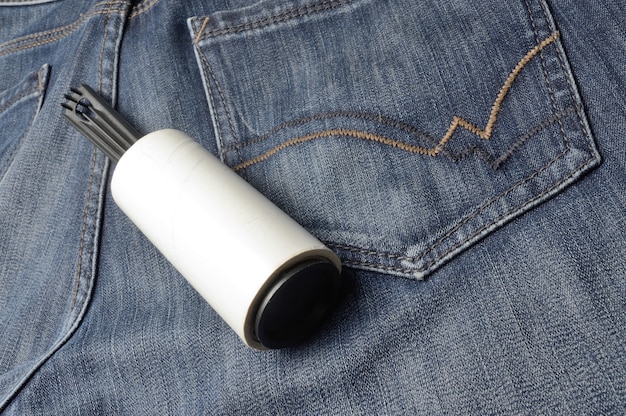 A sticky, roller-coiled garment brush rests on dark jeans.