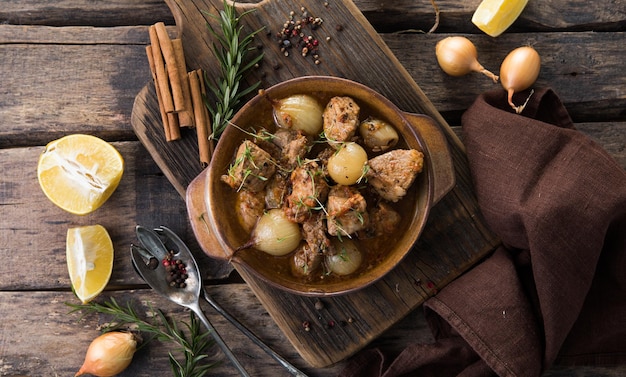 Stifado - delizioso stufato di manzo mediterraneo con bulbi di cipolla, cannella e spezie in una casseruola, su un tavolo di legno nero, vista dall'alto, primo piano