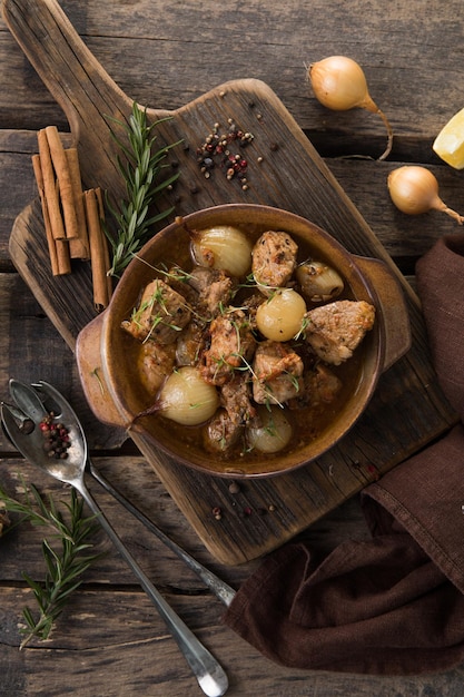 Stifado - delicious mediterranean beef stew with onion bulbs, cinnamon and spices in a casserole, on a black wooden table, view from above, close-up