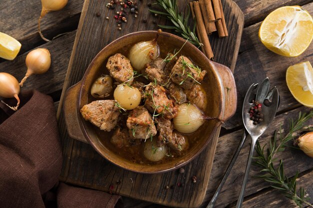 Stifado - delicious mediterranean beef stew with onion bulbs,\
cinnamon and spices in a casserole, on a black wooden table, view\
from above, close-up