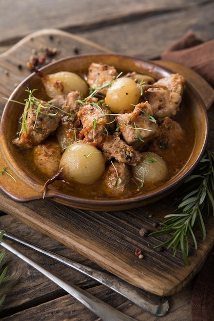 Stifado - delicious mediterranean beef stew with onion bulbs,\
cinnamon and spices in a casserole, on a black wooden table, view\
from above, close-up