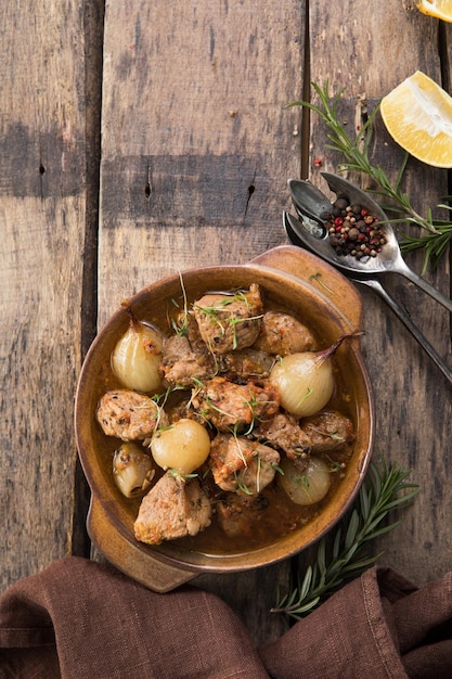 Stifado - delicious mediterranean beef stew with onion bulbs,\
cinnamon and spices in a casserole, on a black wooden table, view\
from above, close-up