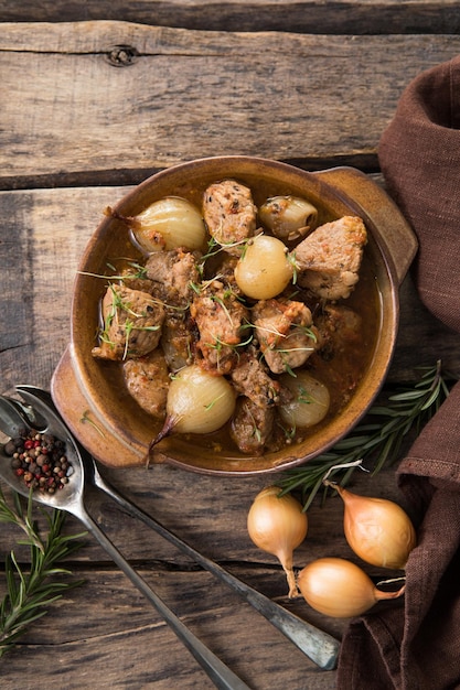 Stifado - delicious mediterranean beef stew with onion bulbs,\
cinnamon and spices in a casserole, on a black wooden table, view\
from above, close-up