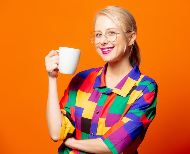 Stijl blond in jaren 90 shirt en bril met een kopje op oranje