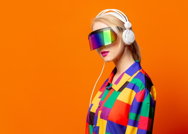 Stijl blonde in jaren 90 kleding met VR-bril en koptelefoon op oranje
