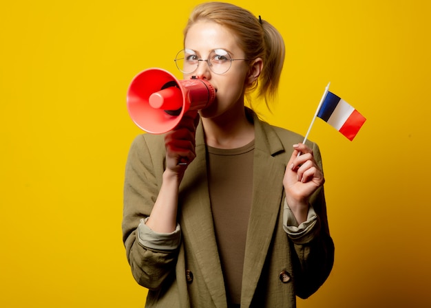 Stijl blonde vrouw in jas met Franse vlag en megafoon op geel