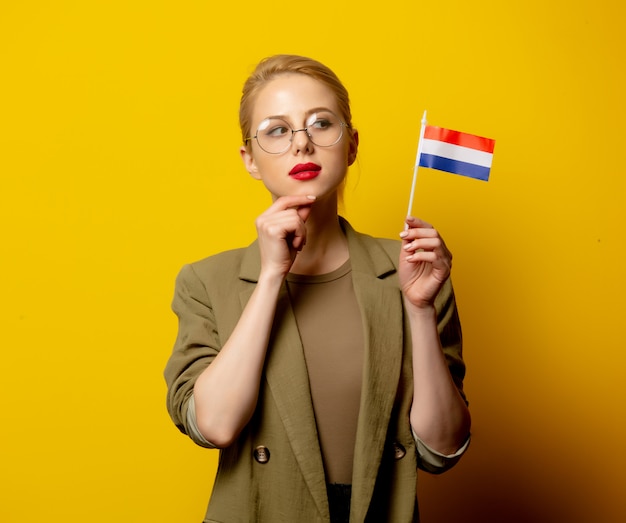 Stijl blonde vrouw in jas met nederlandse vlag op geel