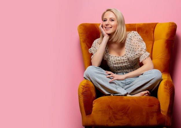 Stijl blonde vrouw zitten in een vintage fauteuil op roze muur