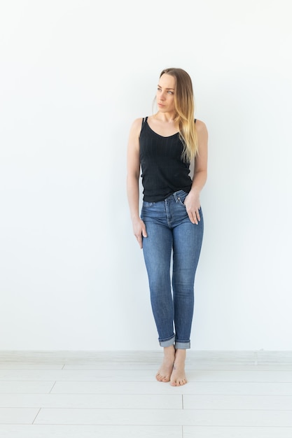 Stijl, mensenconcept - jonge vrouw in jeans en zwart overhemd die zich over de witte muur bevinden