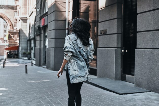 stijl van de stad. achteraanzicht van een jonge vrouw in een spijkerjasje die door de straat loopt