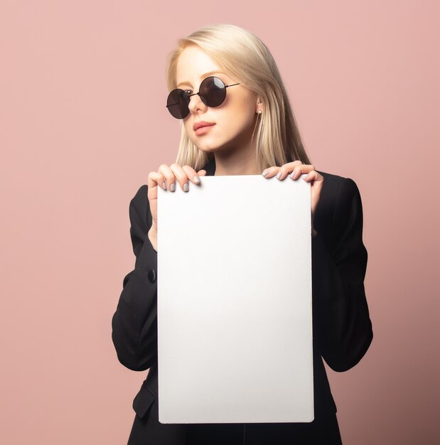 Stijlblonde in blazer en zonnebril met papier op roze achtergrond