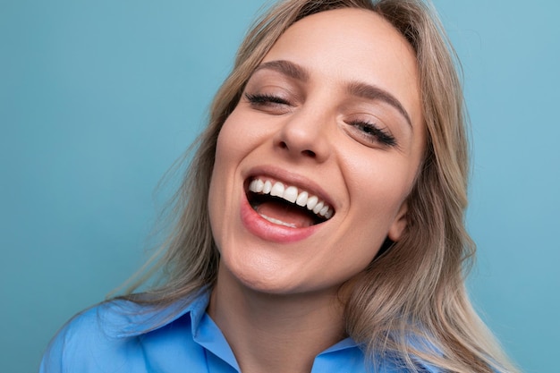 Stijlvol casual blond meisje flirt en glimlacht op een blauwe geïsoleerde achtergrond