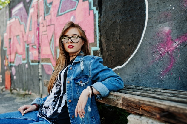 Stijlvol casual hipster meisje in jeans slijtage en bril tegen grote graffiti muur.