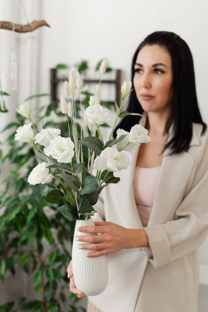 Stijlvol donkerbruin meisje in een licht jasje met een vaas met bloemen