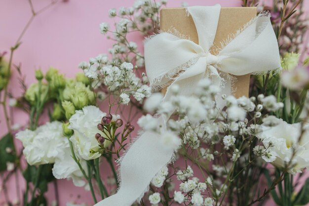 Foto stijlvol eenvoudig cadeau met lint en mooie tedere bloemen op roze achtergrond plat leggen happy womens day en mother's day concept floral wenskaart of banner