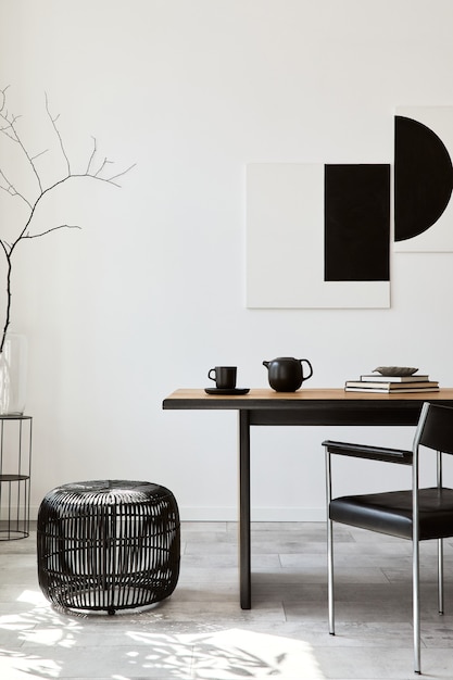 Stijlvol eetkamerinterieur met design houten familietafel, zwarte stoelen, theepot met mok, mock-up kunstschilderijen aan de muur en elegante accessoires in modern interieur. Sjabloon.