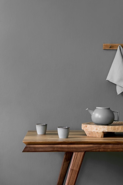 Stijlvol en minimalistisch eetkamerinterieur met houten tafel, theepot met kopjes, dienblad, kopieerruimte en elegante accessoires in grijs modern interieur.