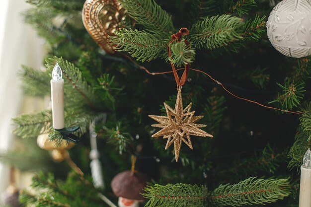 Stijlvol ingerichte kerstboom met vintage gouden kerstballen en kaarsen Sfeervolle wintervakantie voorbereiding Moderne kerstversieringen hangen aan takken close-up