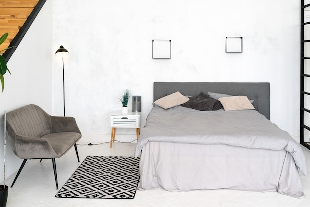 Stijlvol interieur van moderne kamer met comfortabel bed. scandinavisch ontwerp. kamer met bed, fauteuil en zwart-wit vloerkleed op de vloer