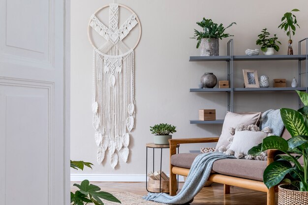 Stijlvol interieur van woonkamer in gezellig appartement met bruine bank, salontafel, boekenstandaard, veel planten, macramé en elegante accessoires. Beige en japandi-concept. Moderne woninginrichting.