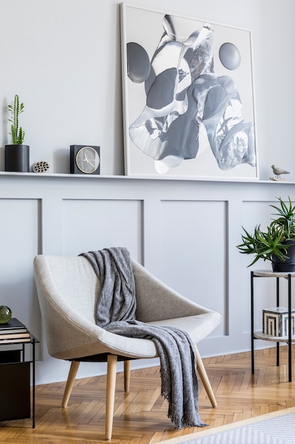 Stijlvol interieur van woonkamer met design grijze fauteuil, kussens, salontafel, schilderijen, plant, decoratie, zwarte klok en elegante persoonlijke accessoires in modern interieur.