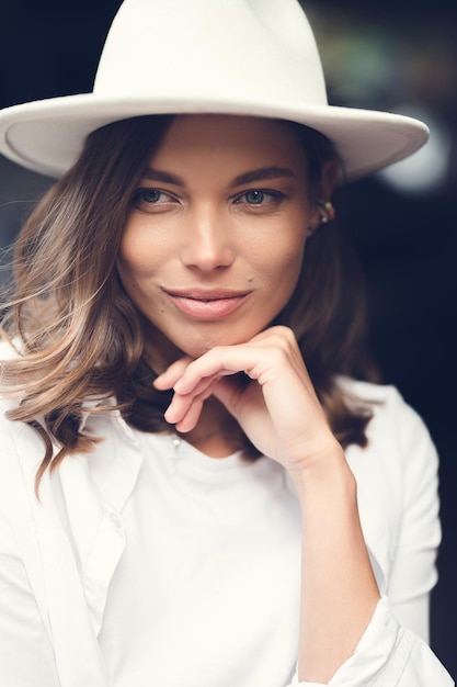 Stijlvol meisje in witte broek en witte katoenen blouse poseren tegen de muur