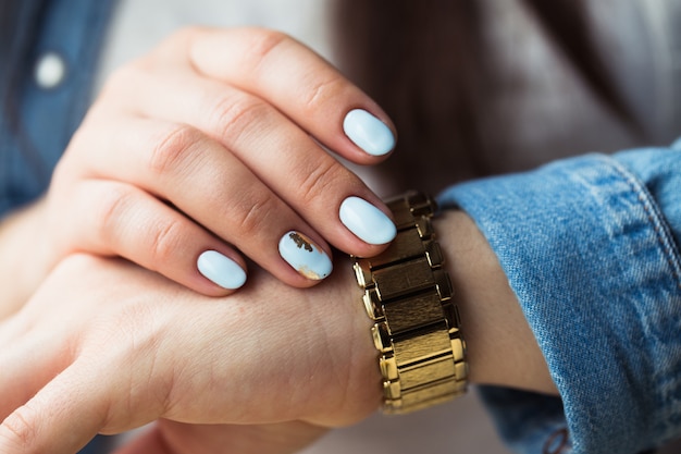 Stijlvol meisje met een blauwe manicure en een gouden klok.