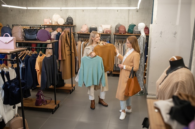 Stijlvol meisje overleggen met haar moeder tijdens het kiezen van nieuwe trui voor de lente in afdeling trendy kleding tijdens het winkelen